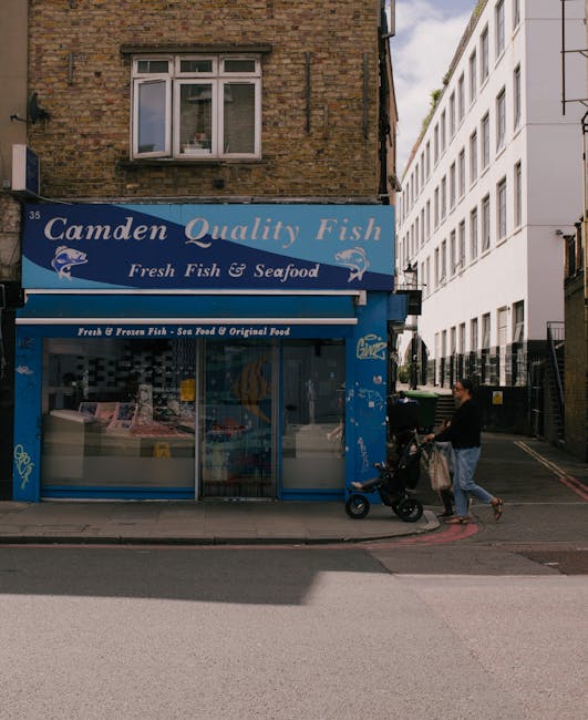 A city street scene at Camden Road in Kentish Town during daylight, showing a building facade with various graffiti and street art, including a large white and gray piece on the upper wall and a color