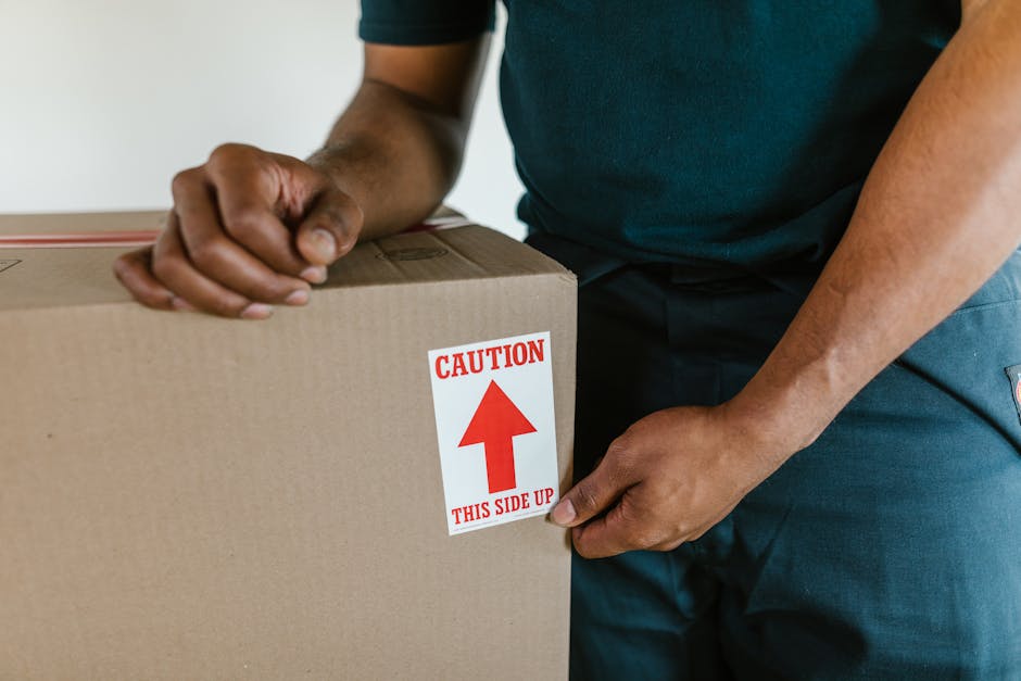 Inside a room prepared for a home relocation, a white sofa covered with a protective sheet is positioned on the left side of the image, while three cardboard boxes of various sizes, sealed with packin